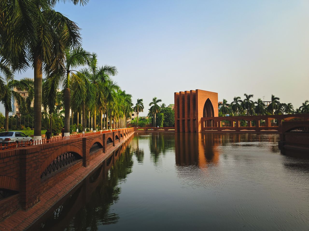 Peaceful scene of palm trees and architecture reflected in calm water.
